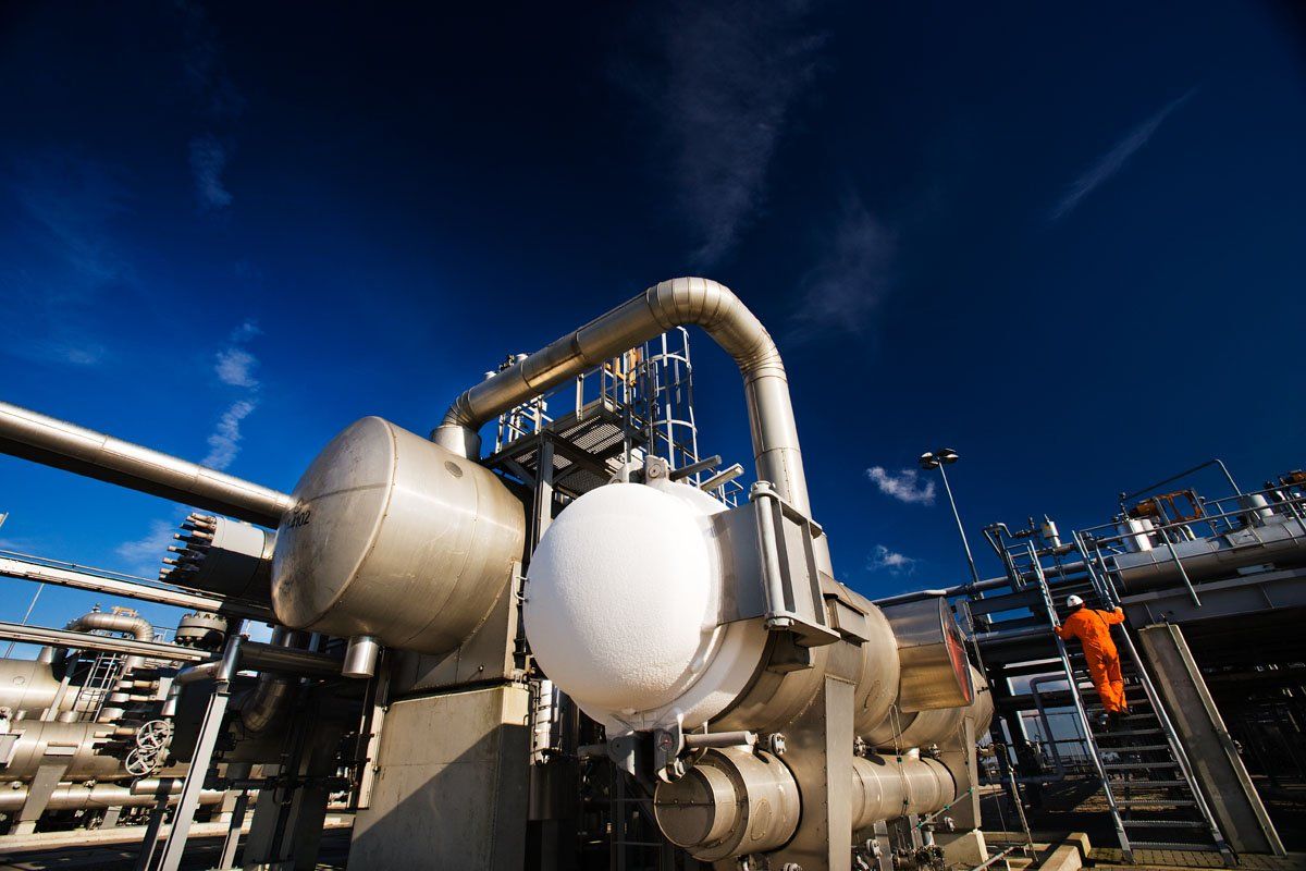 Industriële installatie met grote metalen tanks en leidingen onder een blauwe hemel bij schemering