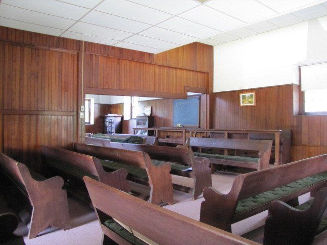 Wooden pews face a stage with a mirror and small screen. The room has wood paneling.