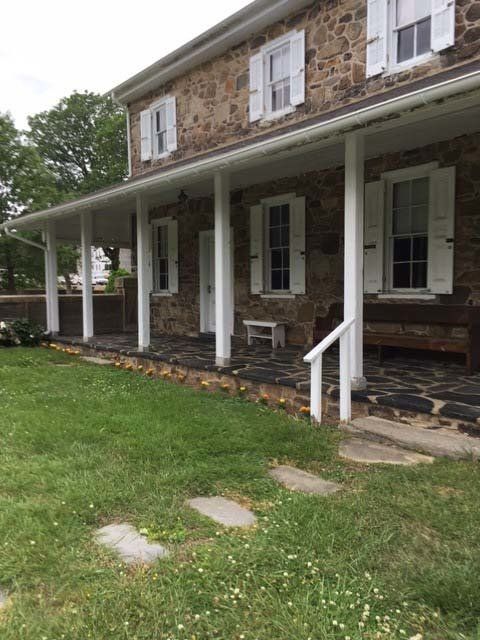 Stone house with porch, white columns, shutters, and a grassy yard.