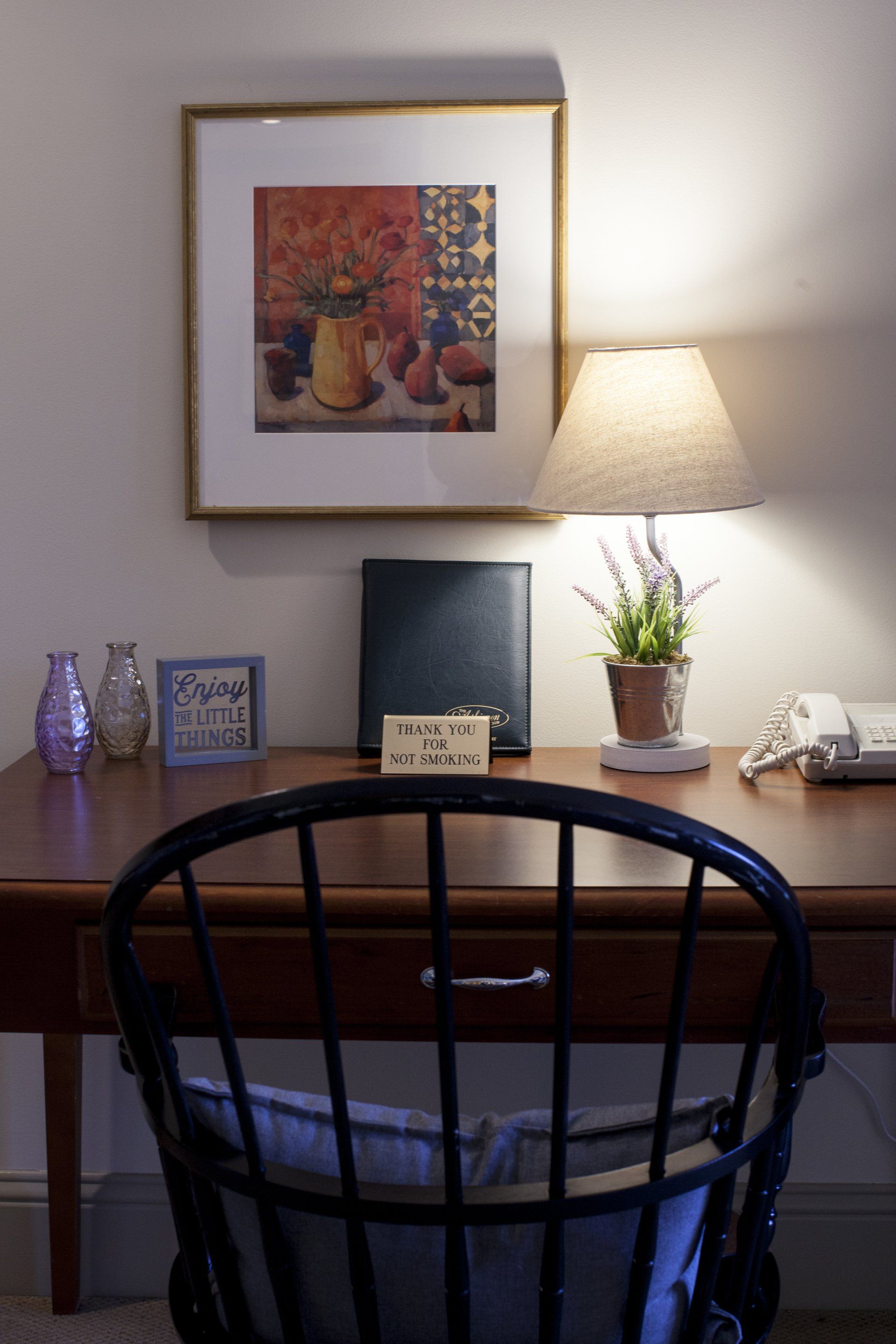 Desk in the Fildstone Suite with a purple glass vase, framed sign, plant, phone and lamp.