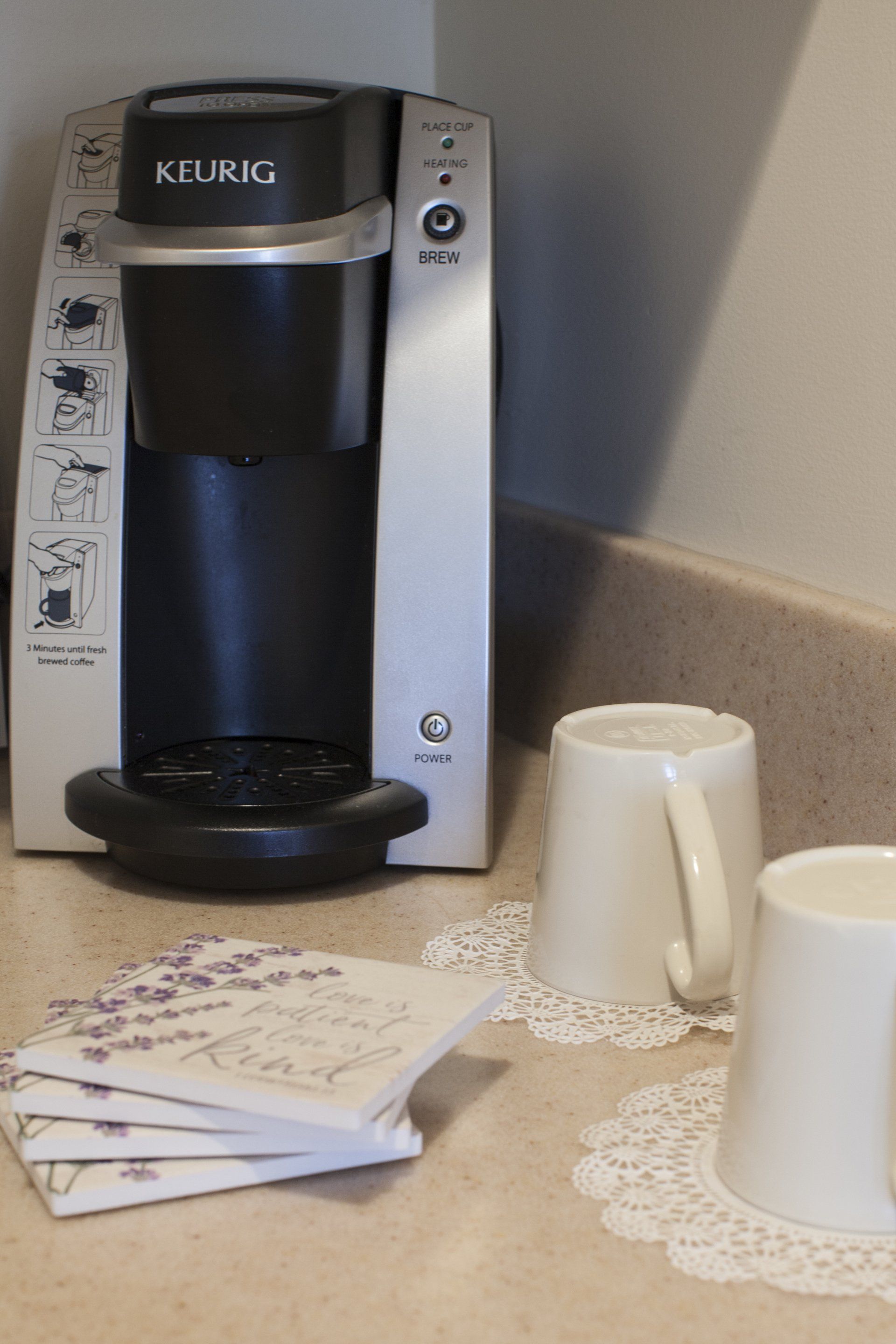 Close up photo of  Kuerig machine with a coffee cup face down on a white doily.