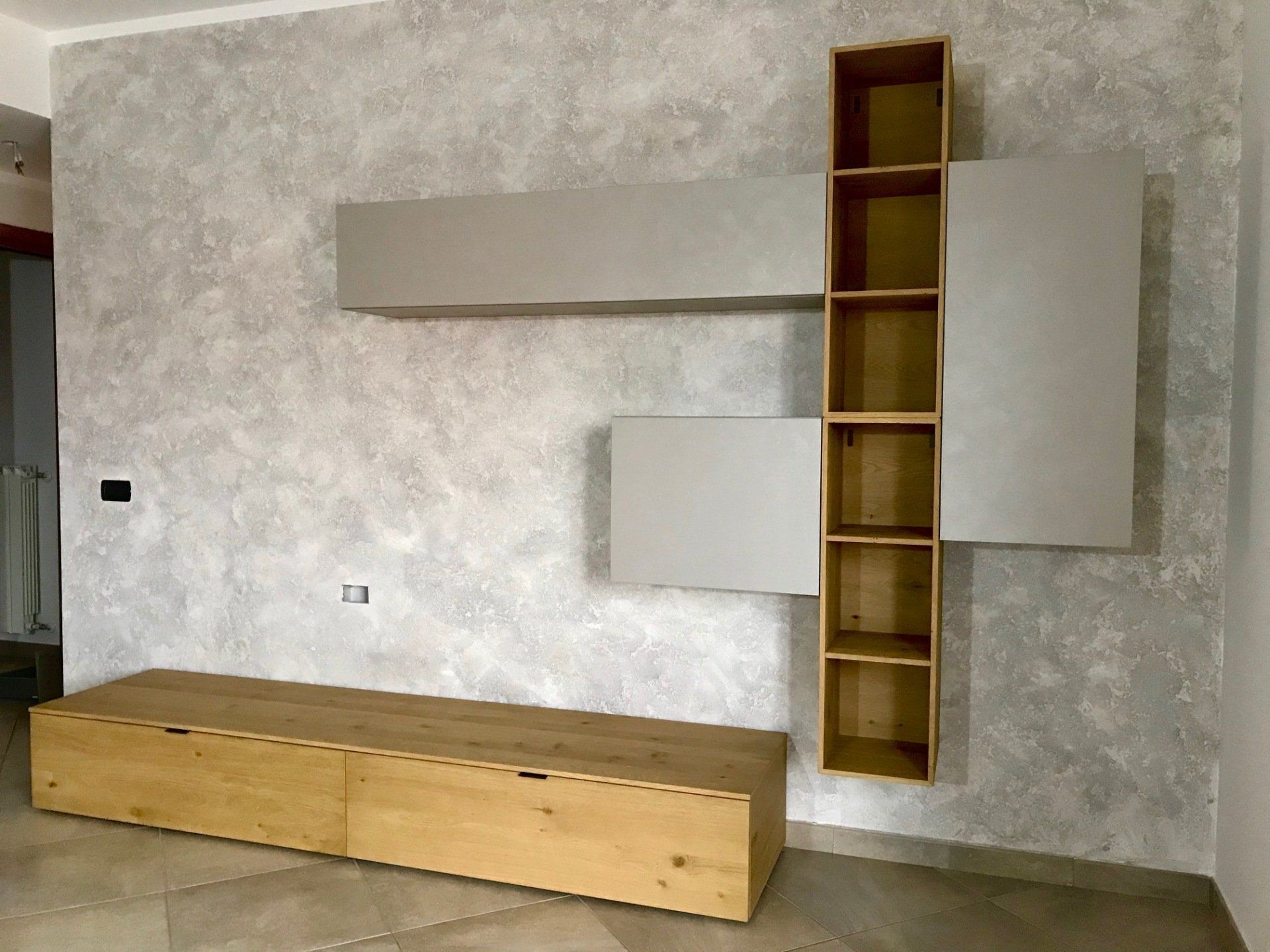 Consolle multimediale sospesa in legno e mobili a parete contro una parete grigia testurizzata.