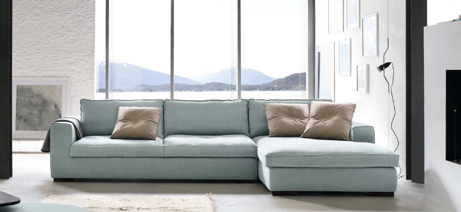 Divano componibile azzurro con cuscini beige in un soggiorno moderno con vista sulle montagne.