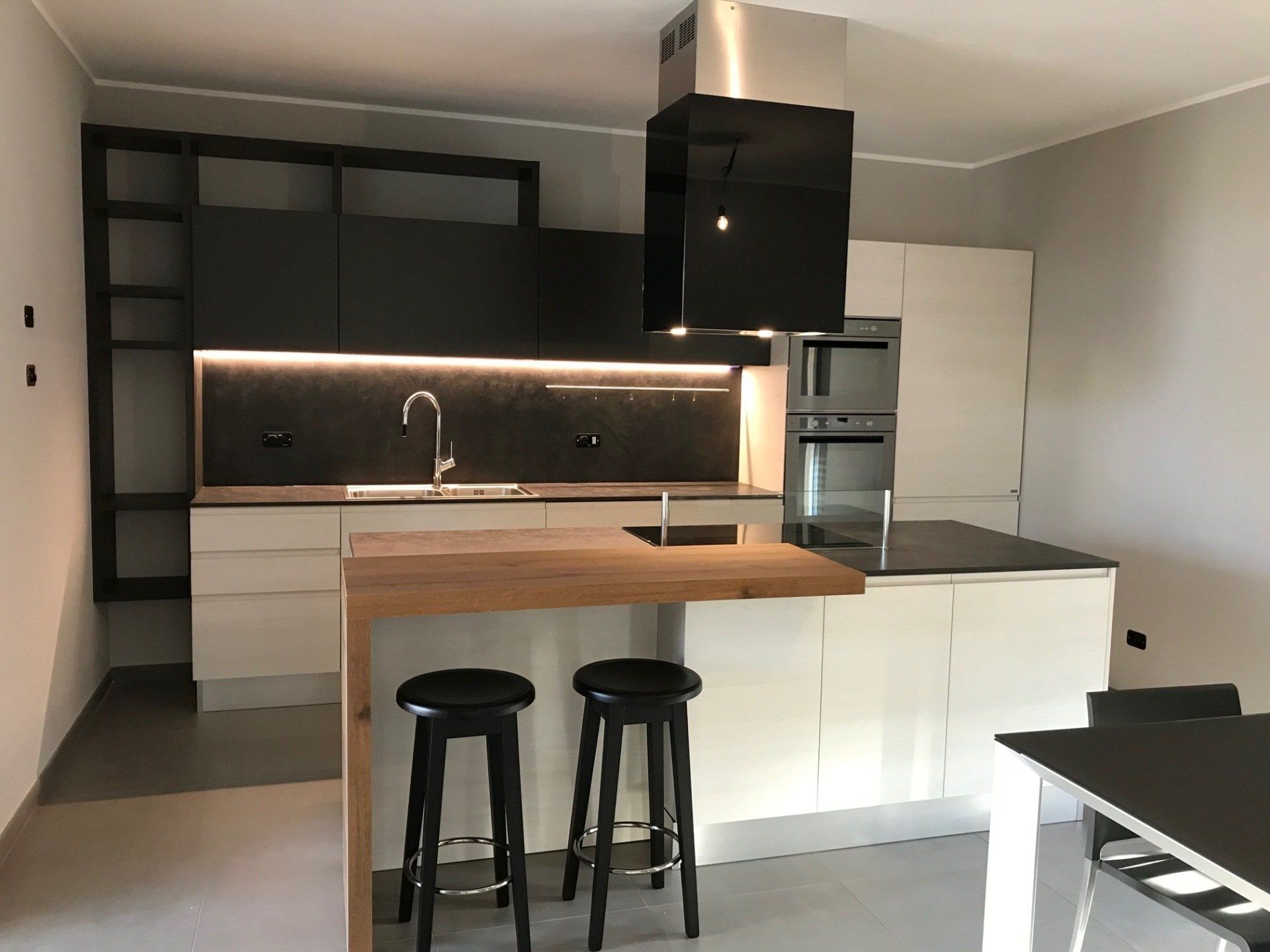 Cucina moderna con mobili bianchi, dettagli neri, isola in legno con sgabelli ed elettrodomestici in acciaio inossidabile.