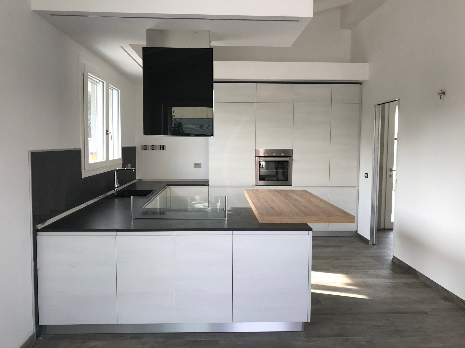 Moderna cucina bianca con ripiani neri, isola in legno e dettagli in acciaio inossidabile.