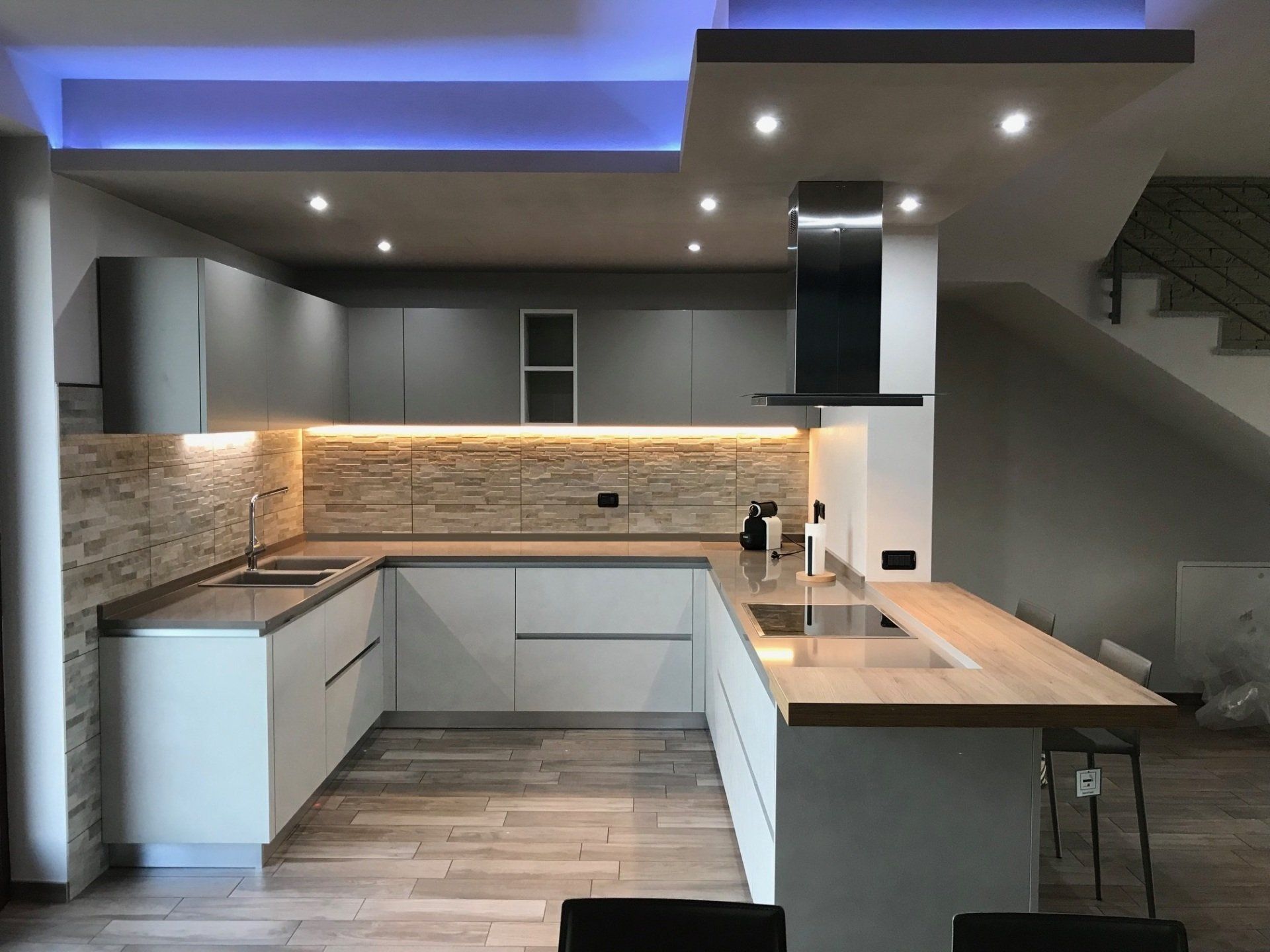 Cucina moderna con mobili grigi, paraschizzi in pietra e isola in legno.