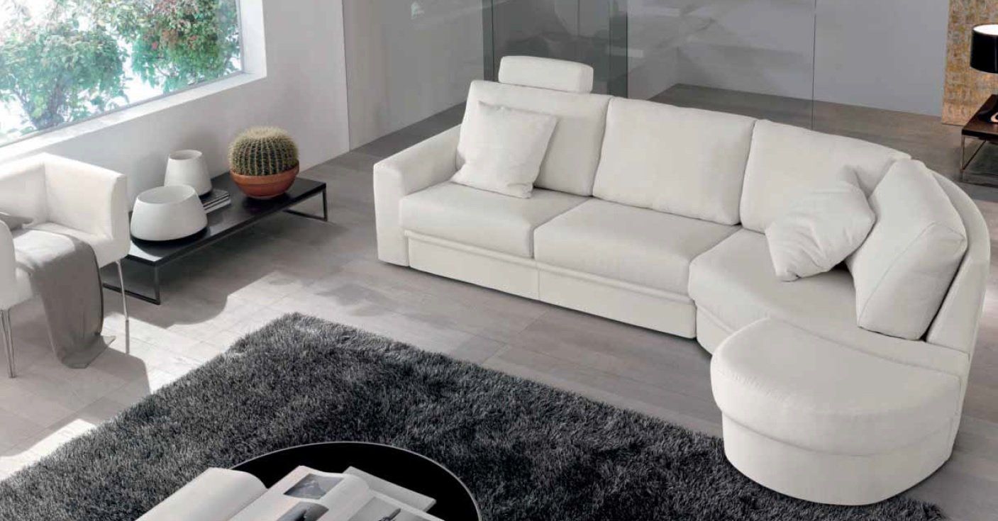 Divano componibile color crema in un soggiorno moderno con tappeto grigio e ampia finestra.