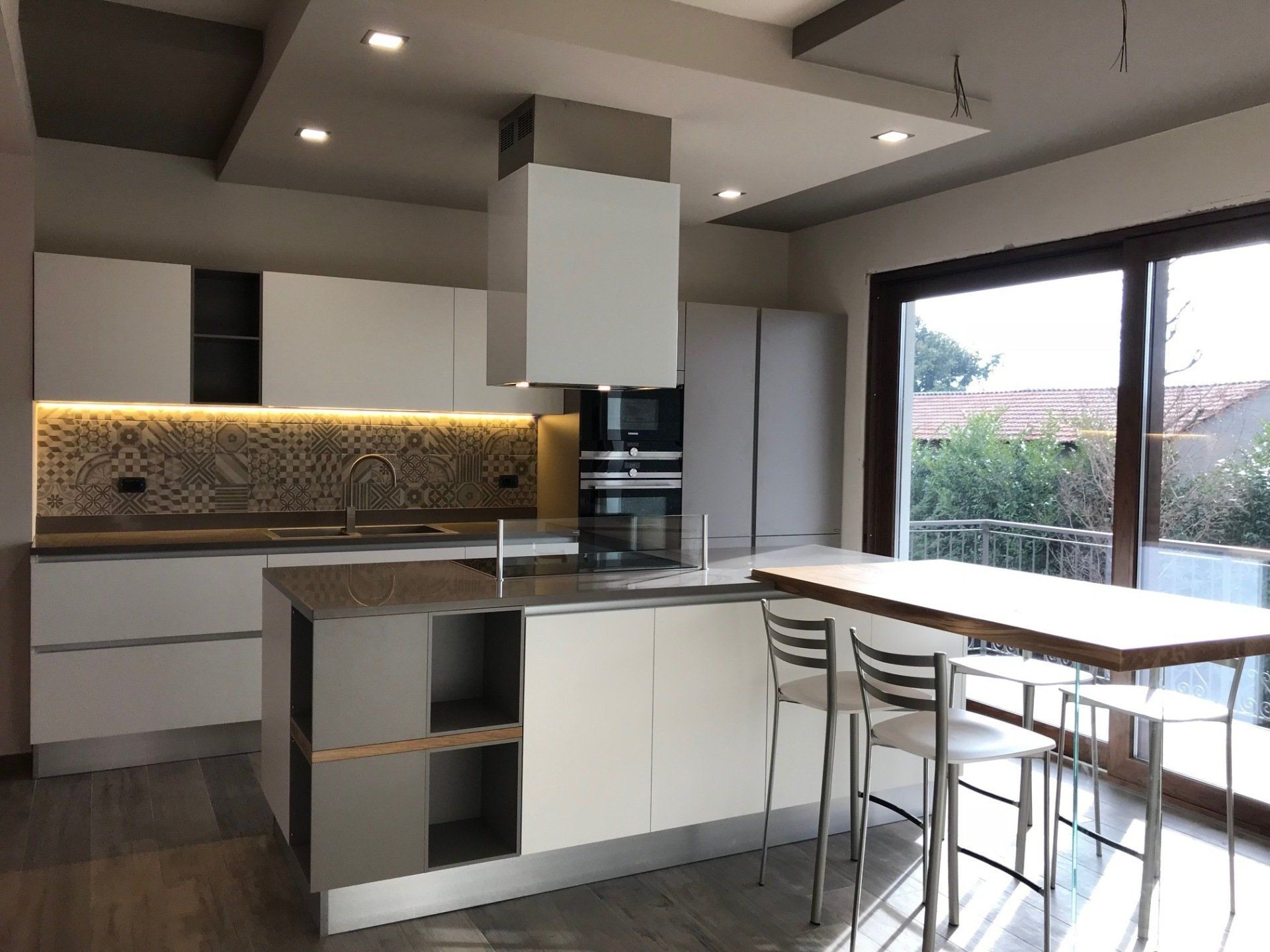 Moderna cucina bianca con isola, elettrodomestici in acciaio inossidabile e tavolo da pranzo in legno.