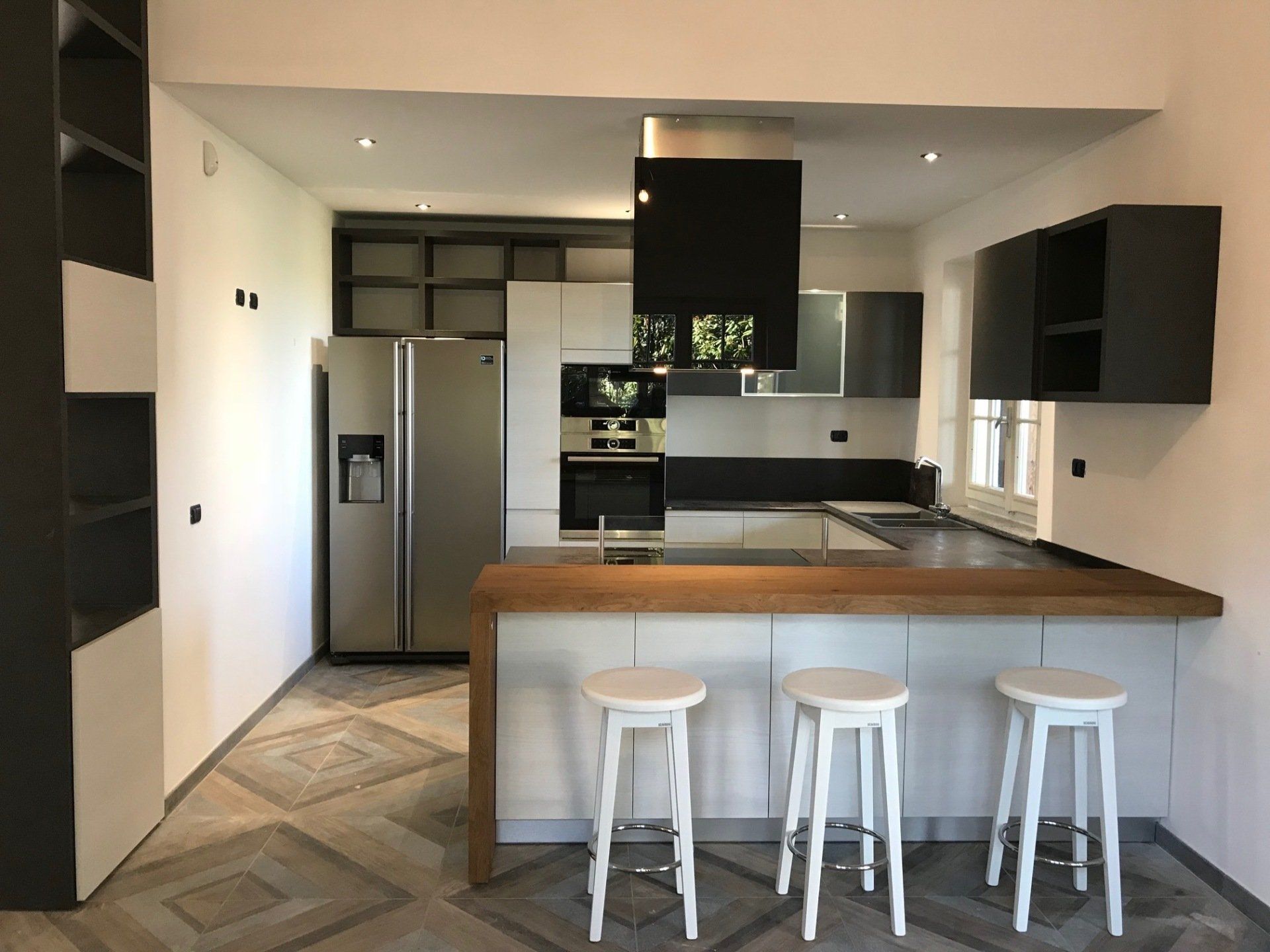 Cucina moderna con mobili bianchi e grigi, isola con sgabelli, frigorifero in acciaio inox.
