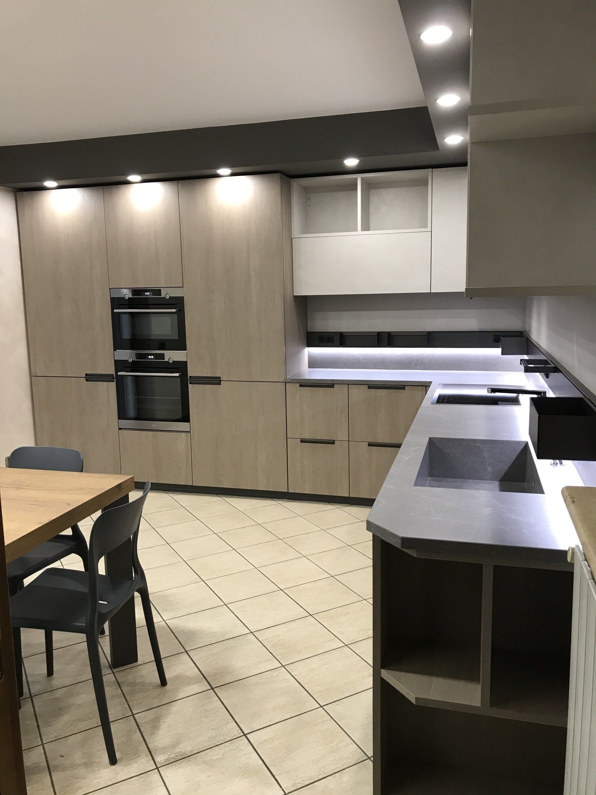 Cucina moderna con mobili in legno chiaro, elettrodomestici in acciaio inossidabile e una piccola zona pranzo.