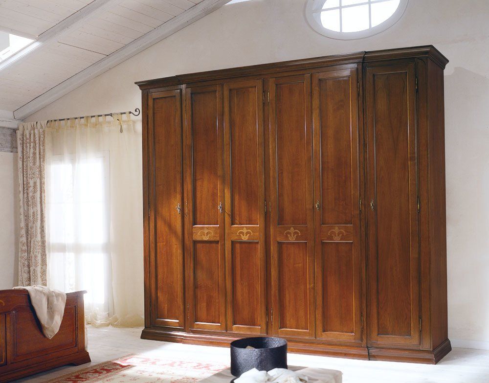 Ampio armadio in legno scuro in una camera da letto luminosa. Comprende sei ante con dettagli decorativi.