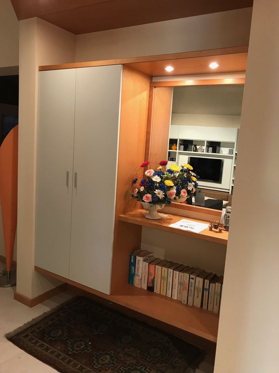 Un ingresso in legno con un mobiletto, uno specchio, uno scaffale con libri e una composizione floreale.