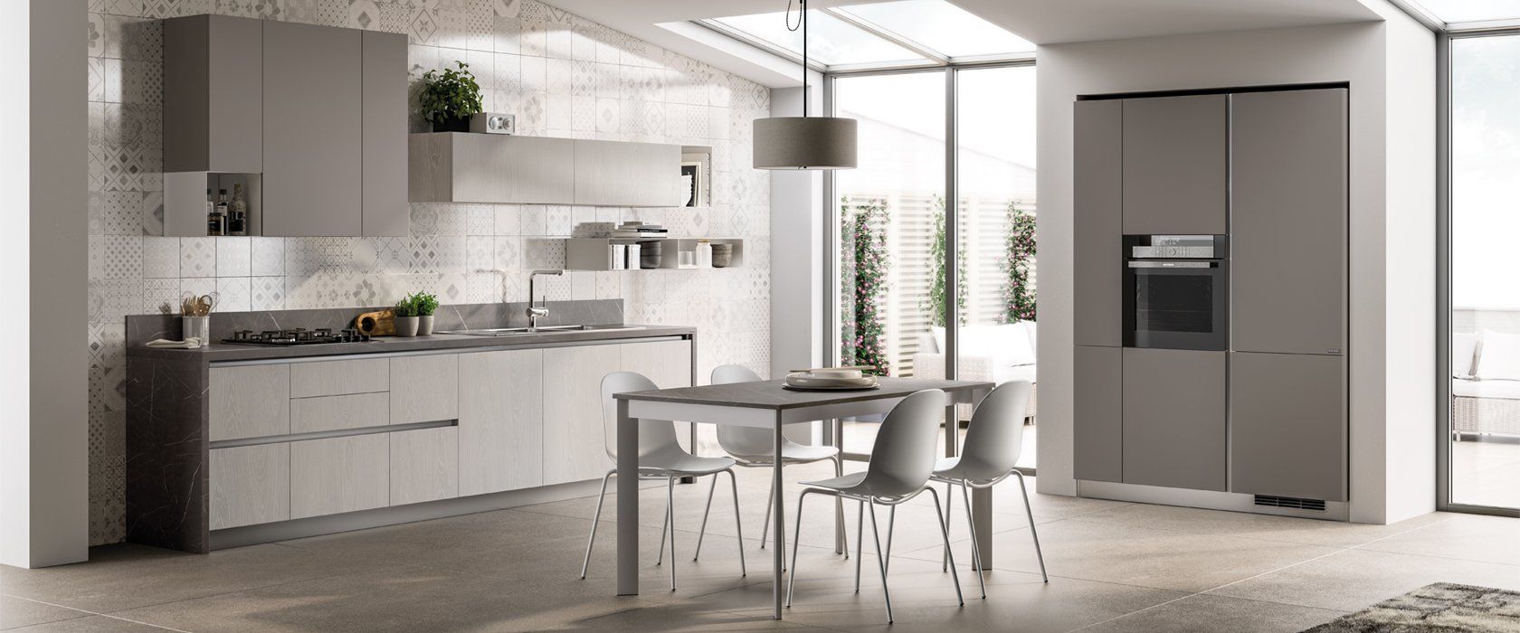 Cucina moderna con mobili grigi, tavolo da pranzo e ampie finestre.