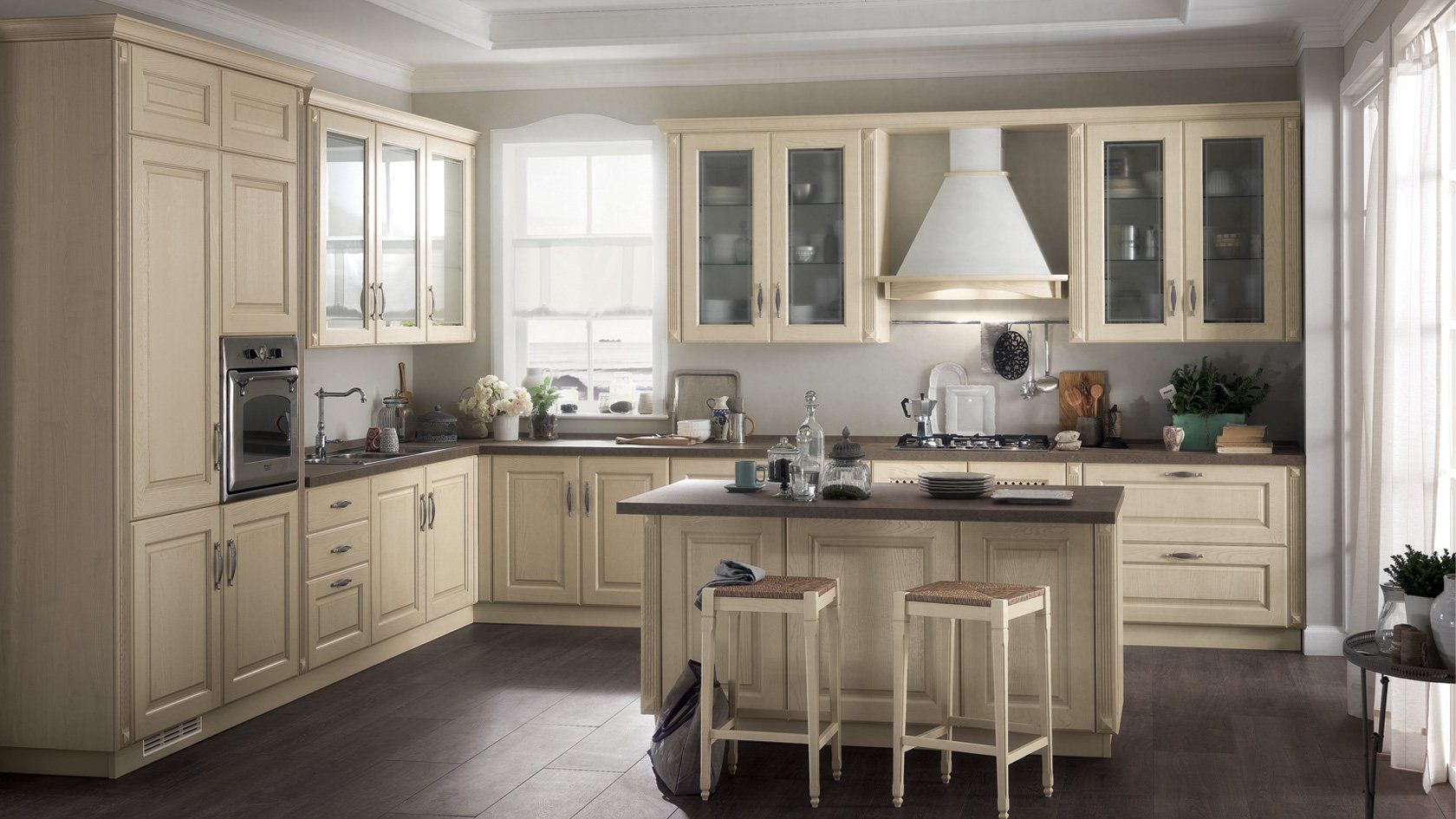 Cucina beige con isola, mobili ed elettrodomestici in acciaio inossidabile. Due sgabelli da bar sono posizionati sull'isola. Pavimento in legno scuro.