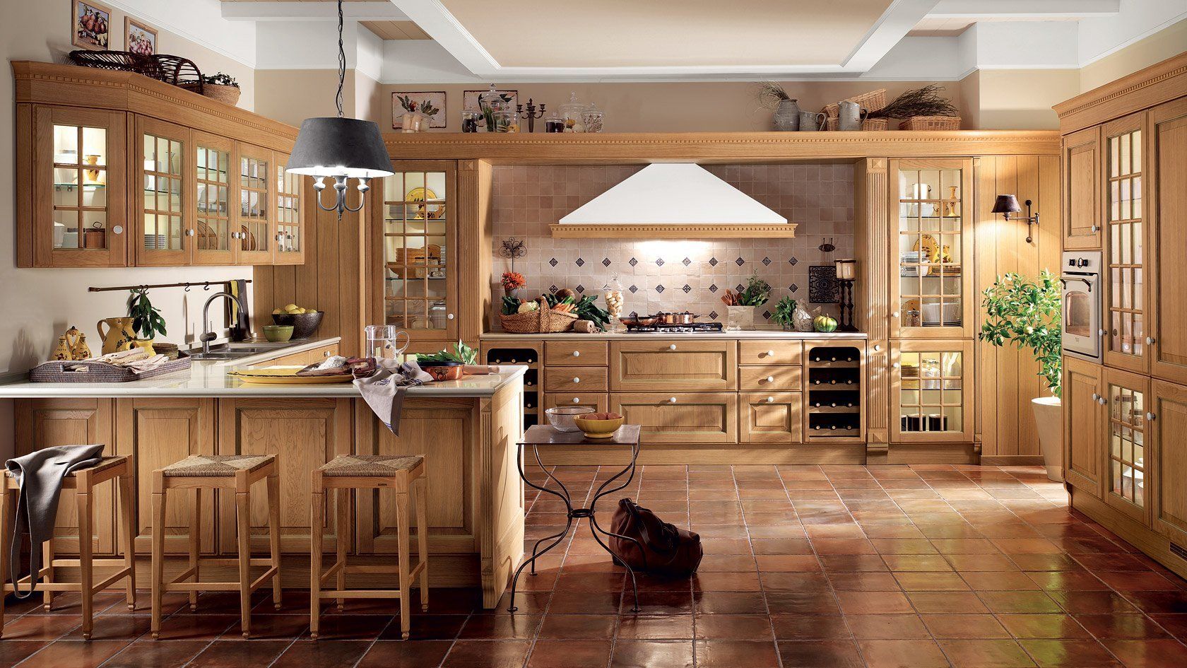 Cucina in legno con isola, mobili ed elettrodomestici; pavimento piastrellato, tonalità legno chiaro.