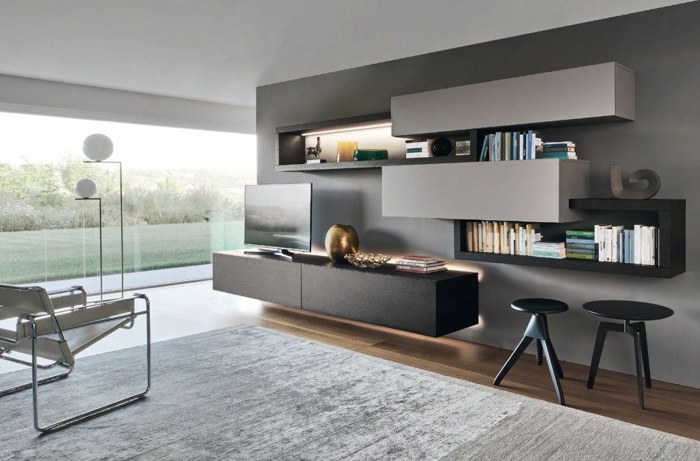 Soggiorno moderno con consolle multimediale sospesa, librerie e sgabelli contro una parete grigia, con ampia finestra e sedia.