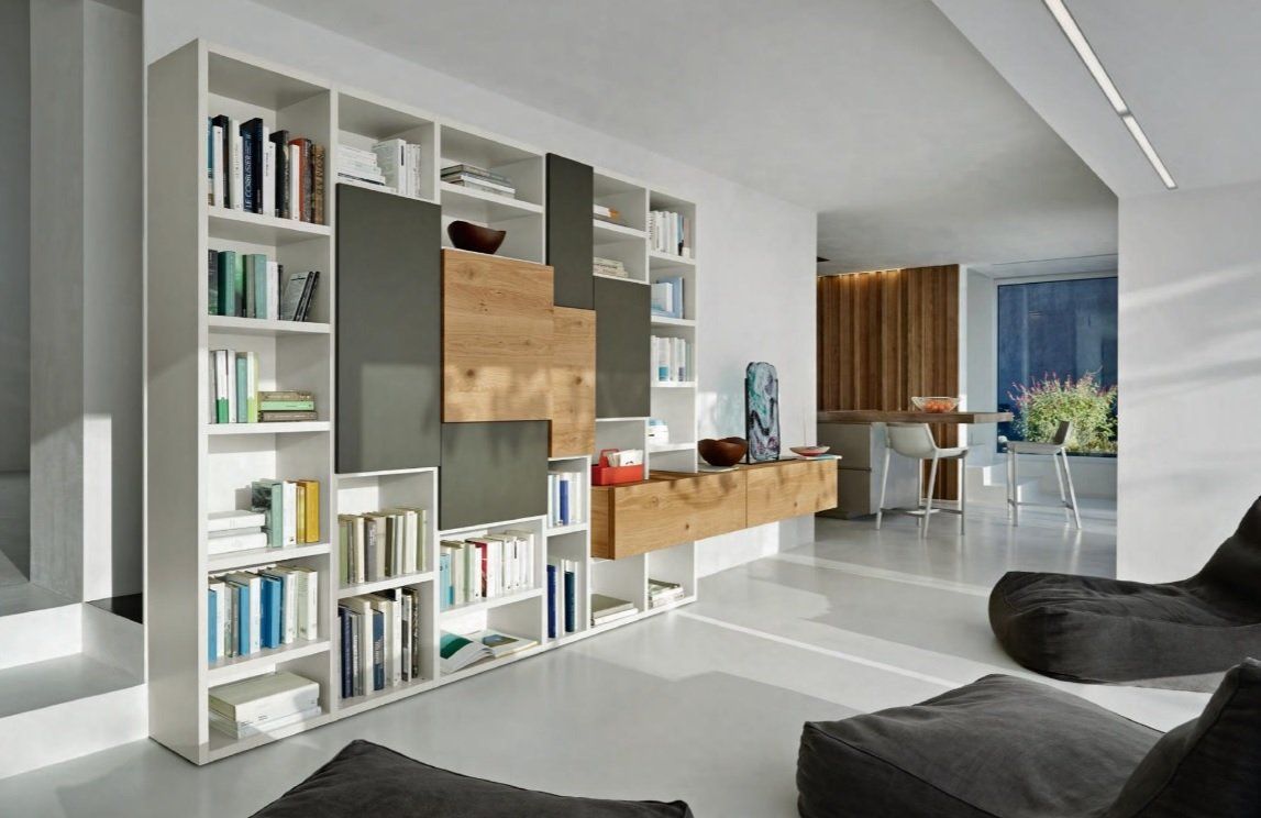Libreria bianca con libri, pannelli in legno e grigi integrati. Luminoso soggiorno moderno con poltrone a sacco.