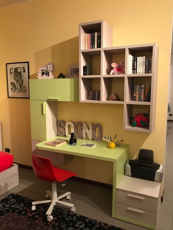 Scrivania moderna con piano verde lime, sedia rossa e scaffalatura integrata, contro una parete gialla.