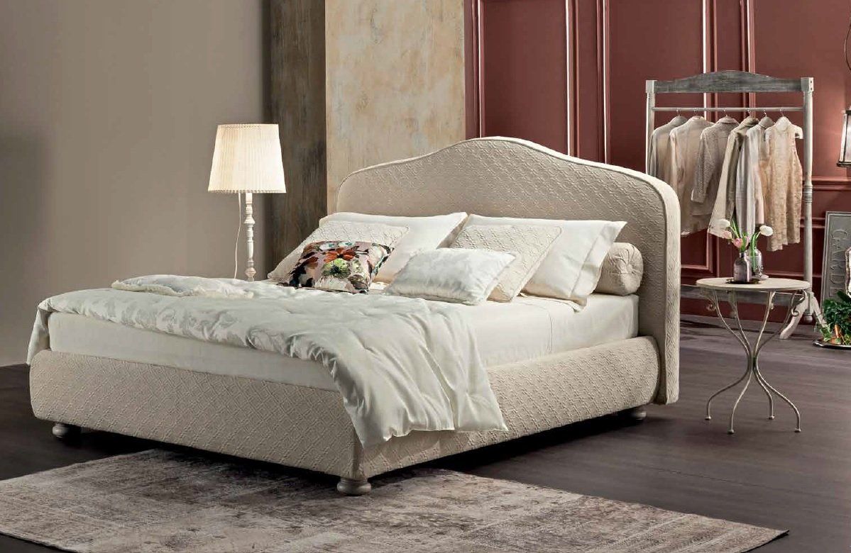 Letto imbottito beige in una camera da letto con tappeto, lampada e appendiabiti.