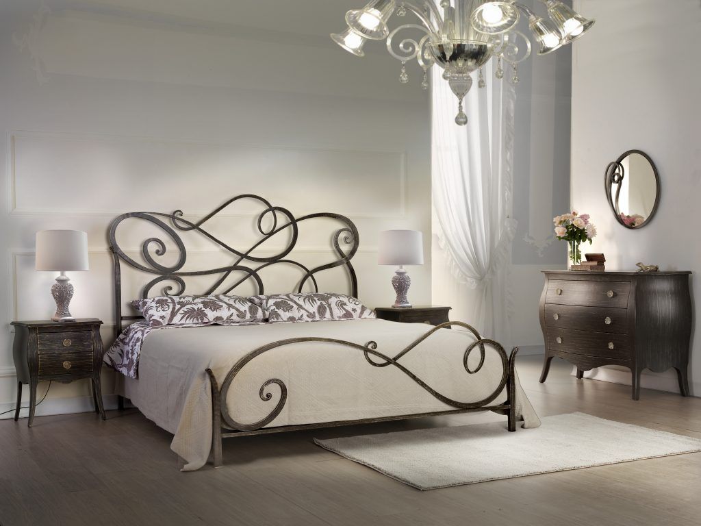Camera da letto con letto in metallo decorato, comodini, cassettiera, tappeto e lampadario.
