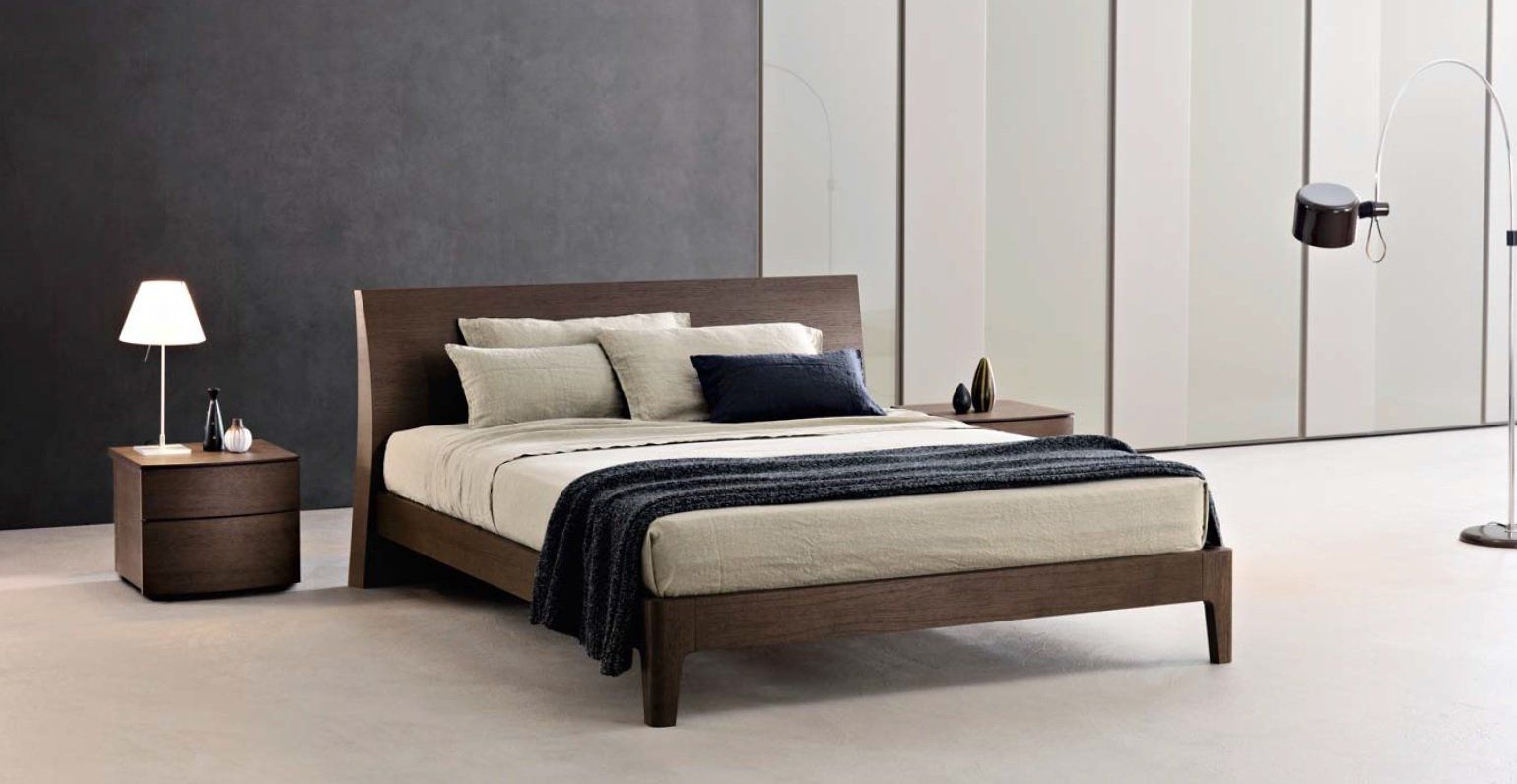 Camera da letto moderna con letto marrone, comodini, lampada e coperta blu scuro.