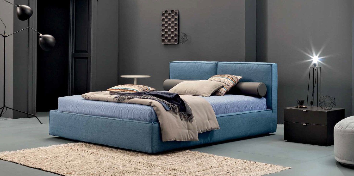 Una camera da letto moderna con un letto imbottito blu, pareti grigie e un soffice tappeto.