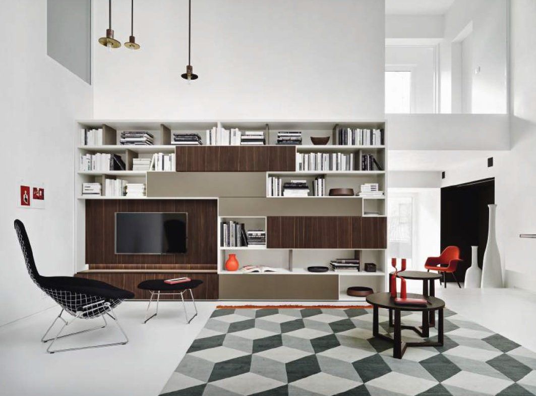 Soggiorno moderno con libreria integrata, TV e tappeto geometrico. Include una poltrona scura e due tavoli neri.