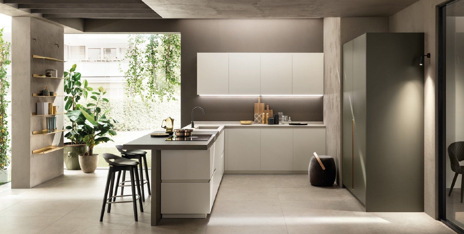 Cucina moderna con mobili bianchi, isola e grande finestra con verde. Sgabelli neri e dispensa alta verde.