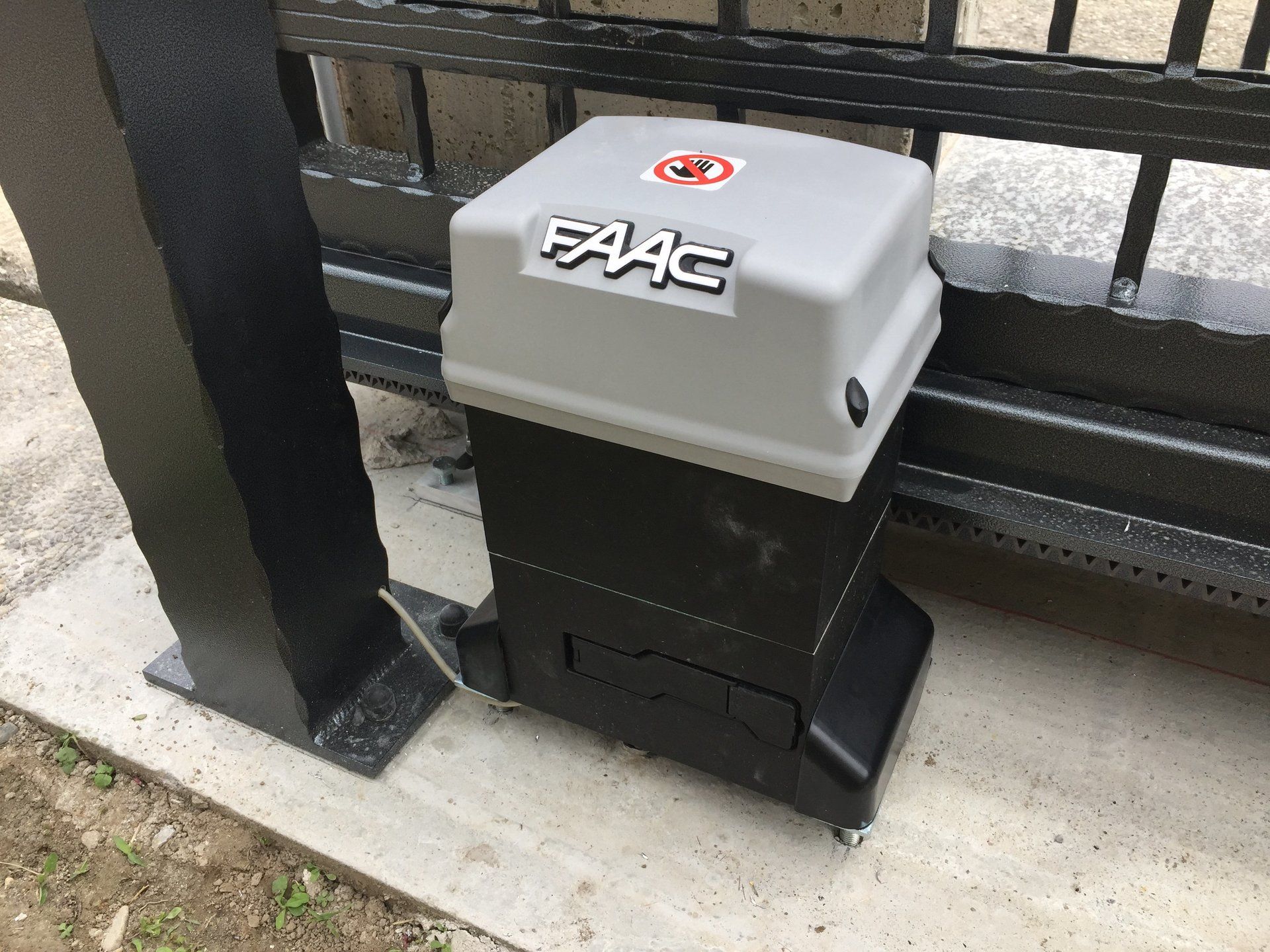 Ein Schiebetormotor sitzt neben einem Zaun.