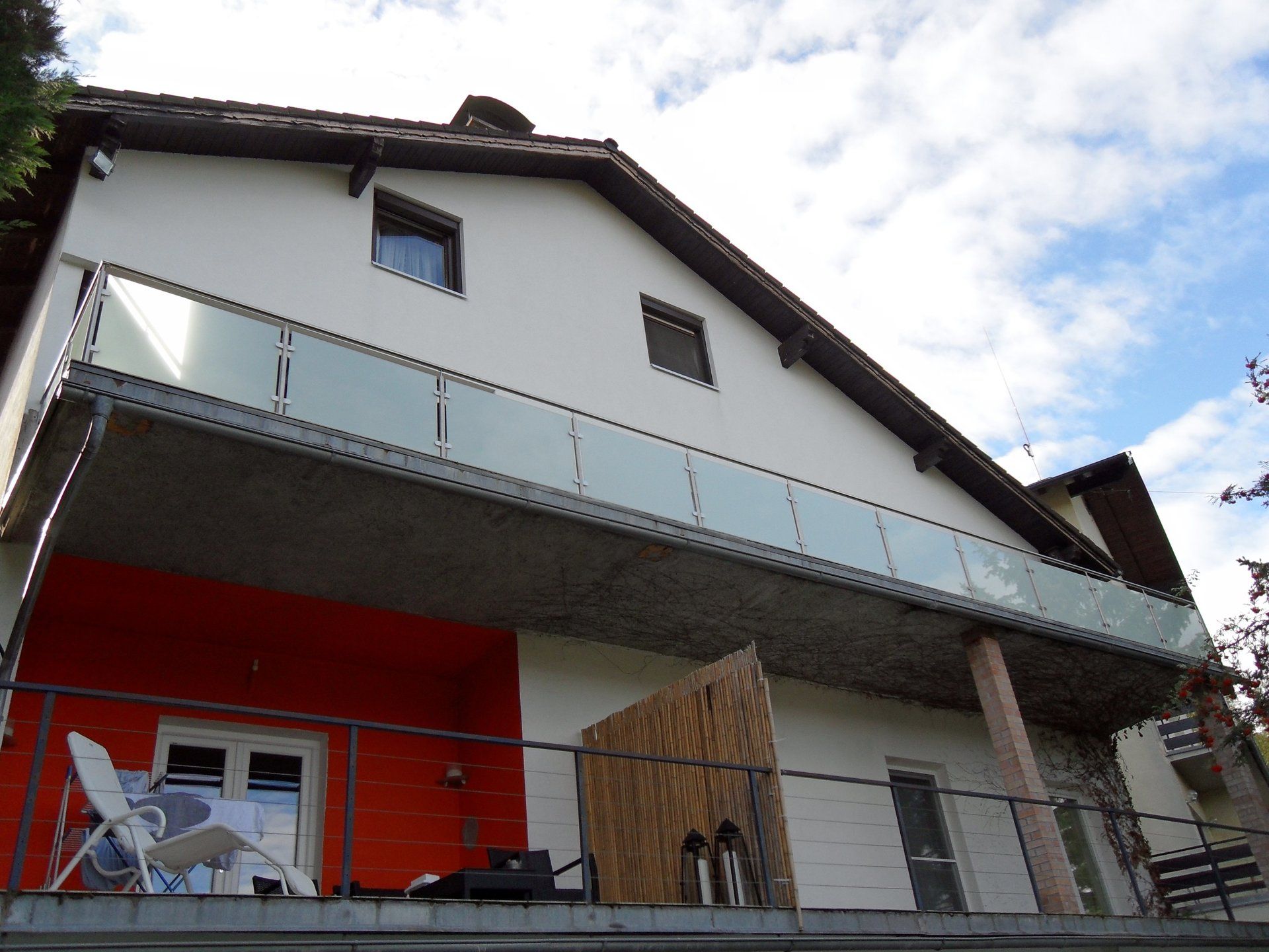 Ein weißes Haus mit einem Balkon mit Glasgeländer