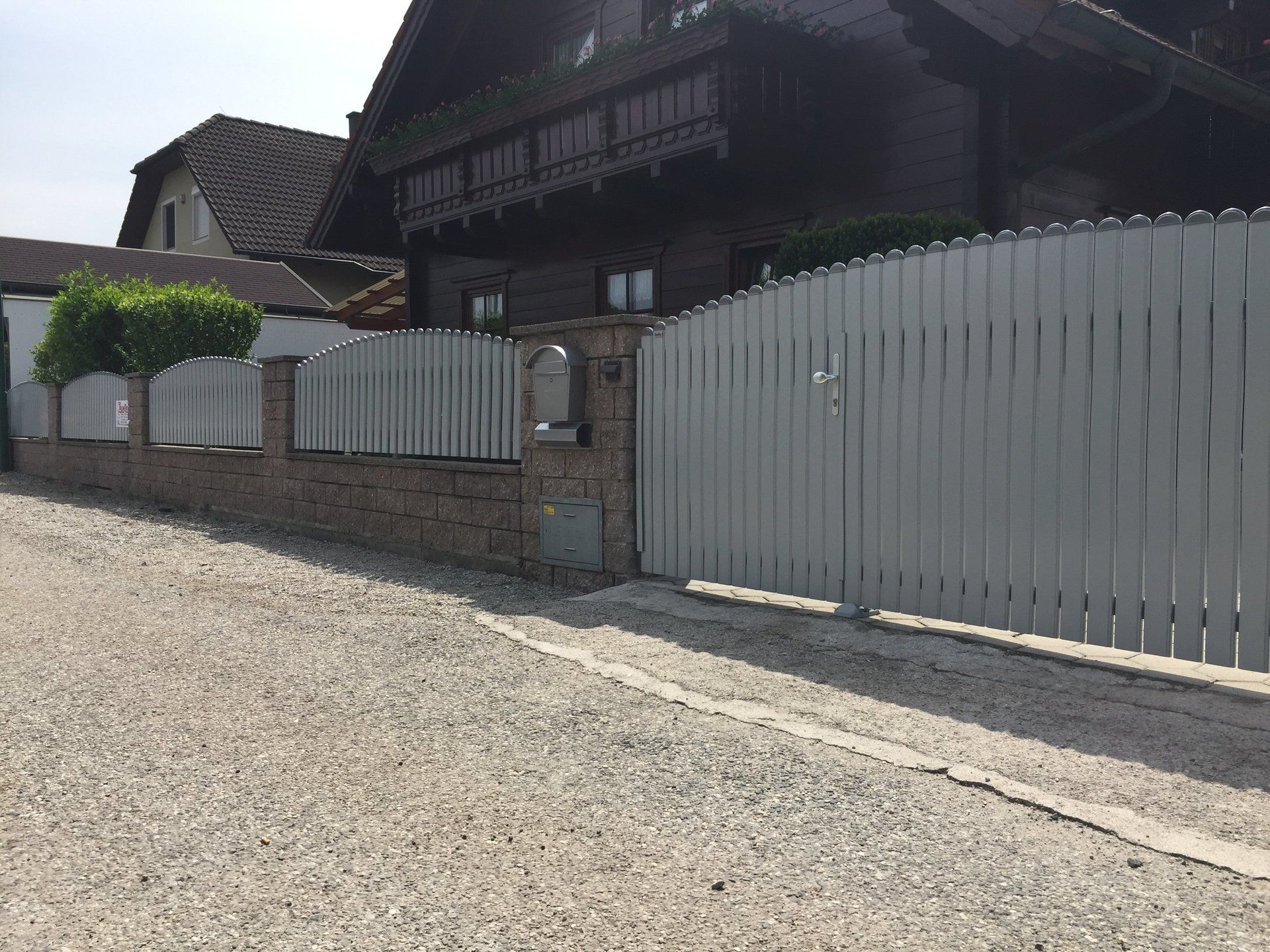 Ein weißer Zaun umgibt ein Haus an einer Schotterstraße.