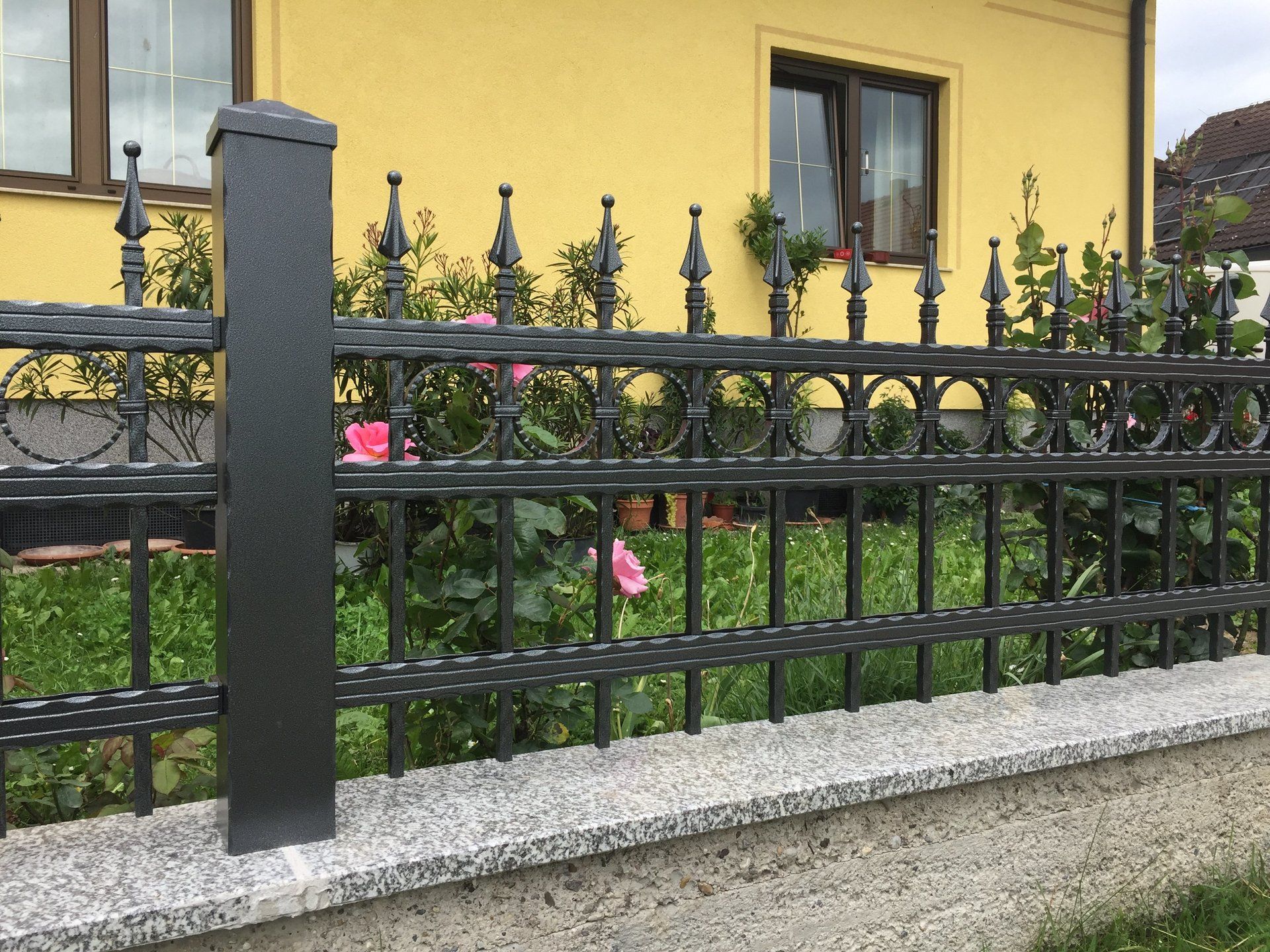 Ein schmiedeeiserner Zaun steht vor einem gelben Haus