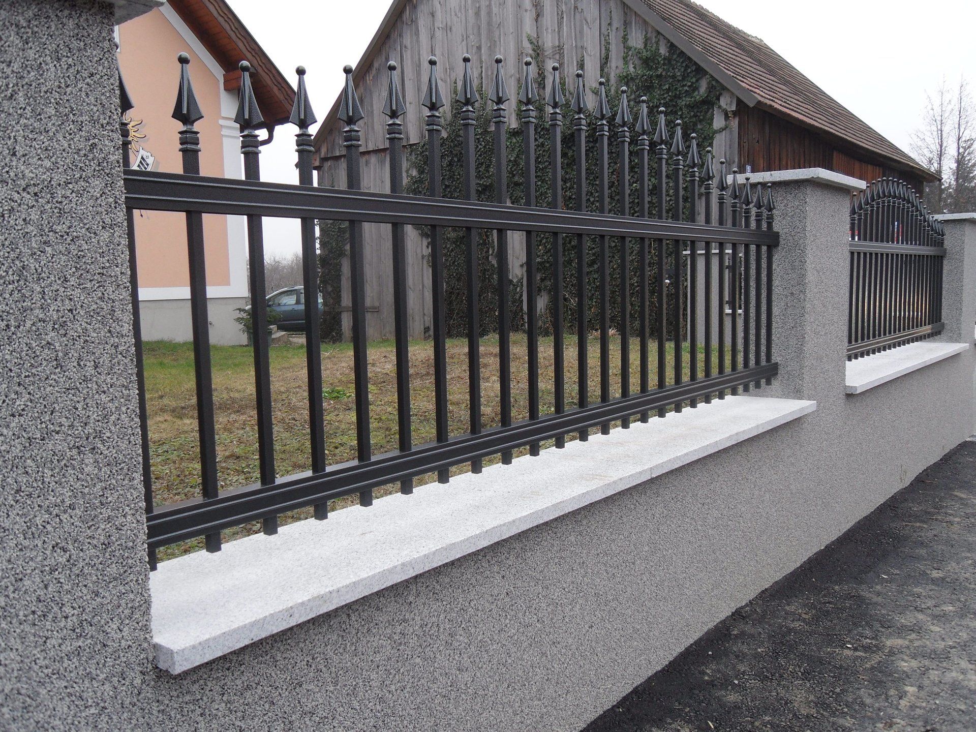 Ein schmiedeeiserner Zaun umgibt eine Steinmauer vor einem Haus