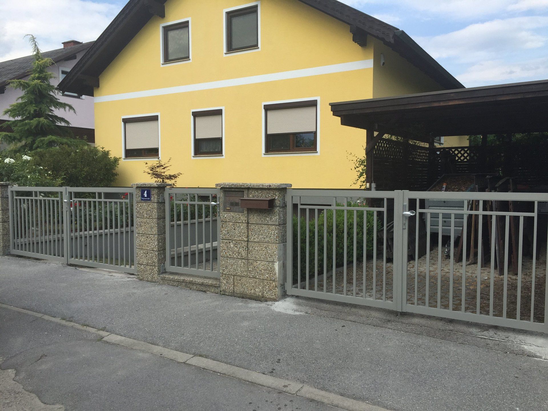 Ein gelbes Haus mit einem Carport und einem Zaun darum