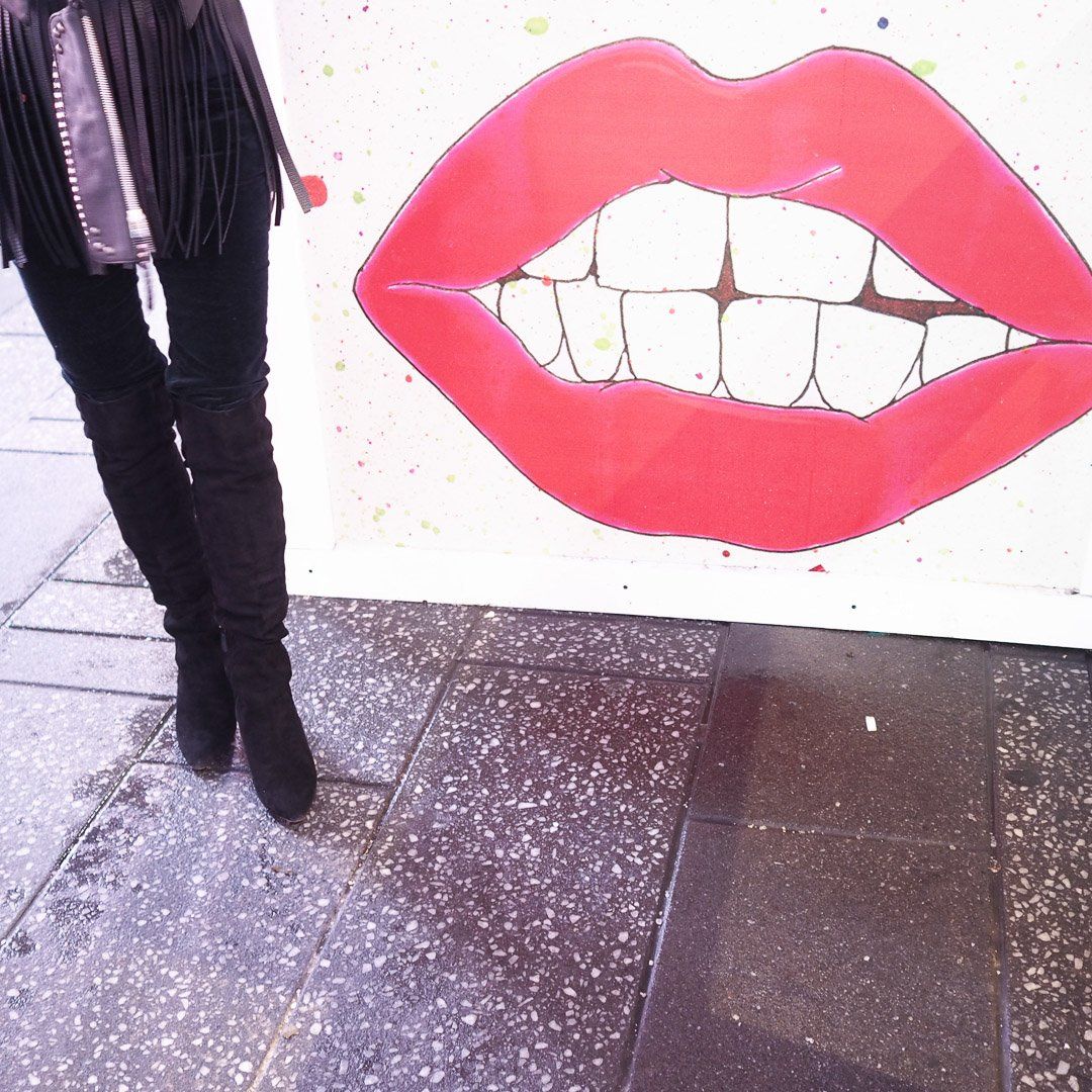 A woman standing in front of a painting of red lips and teeth