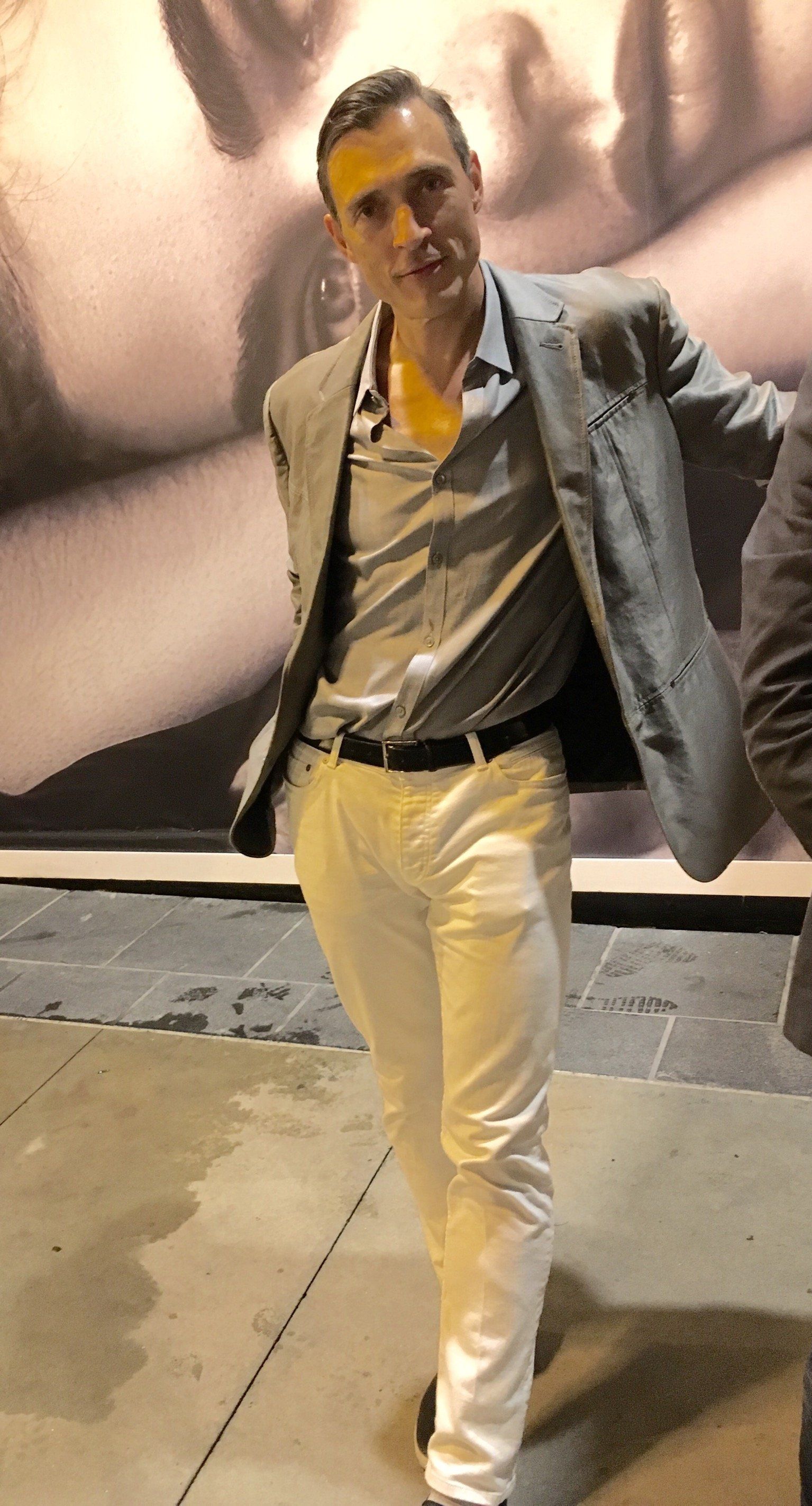 A man in a suit and white pants is standing in front of a large picture.