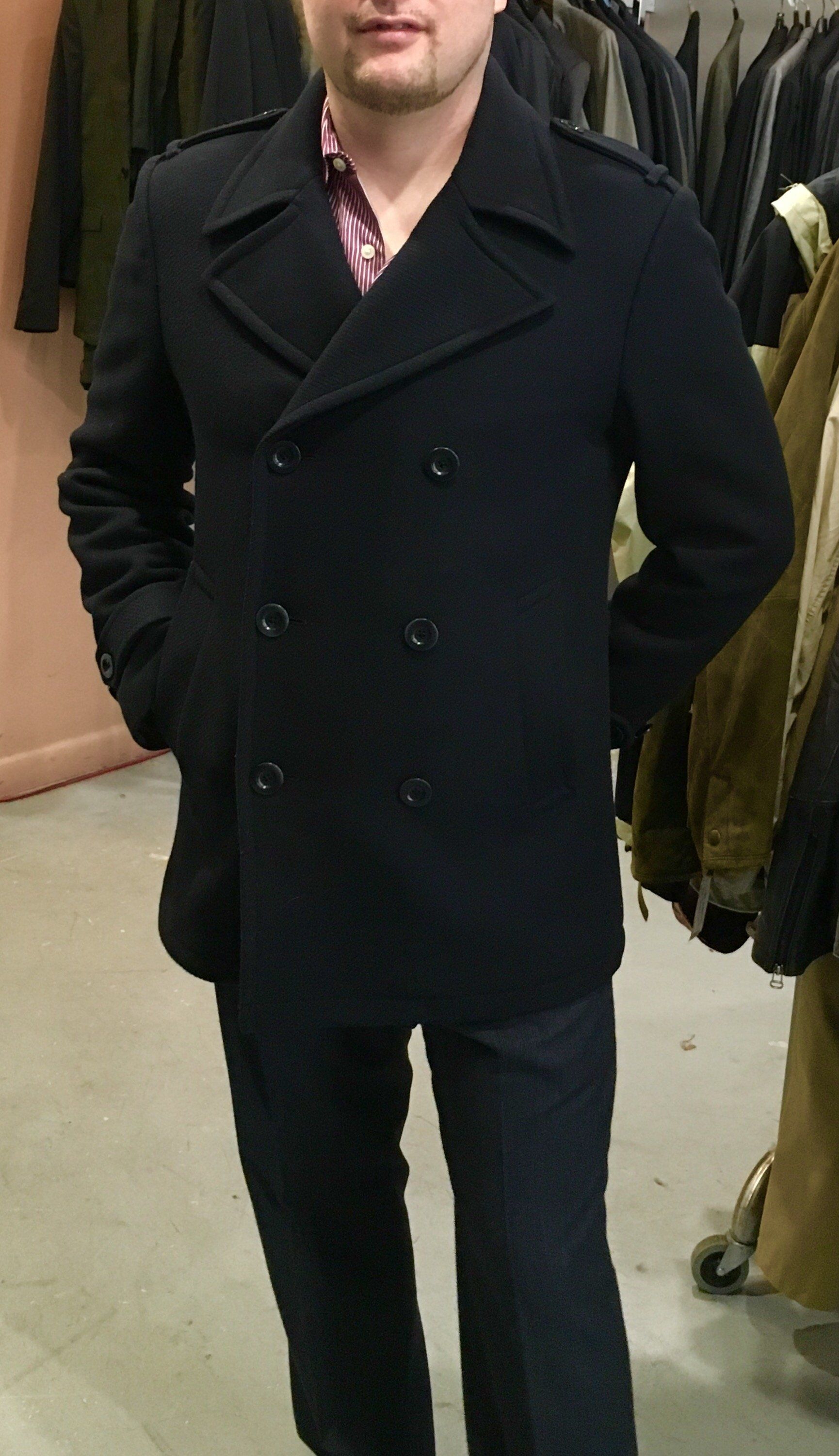 A man wearing a black pea coat is standing in a store.