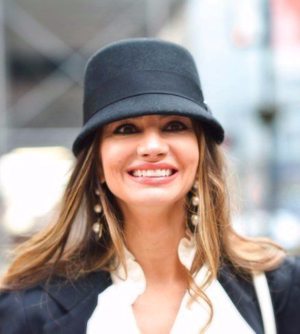 A woman wearing a black hat and earrings smiles for the camera