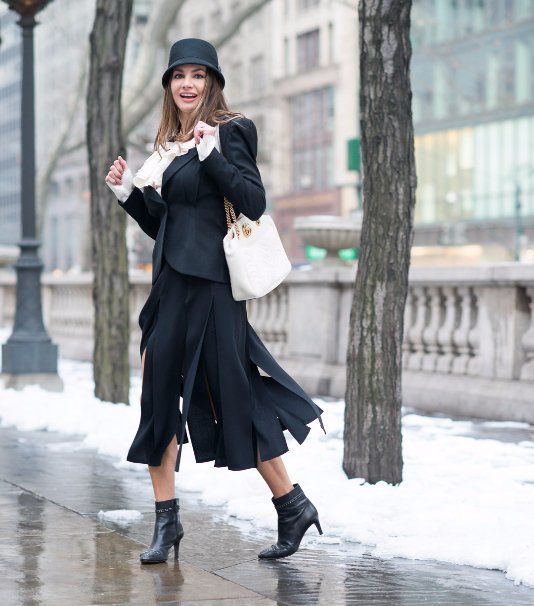 A woman wearing a black hat and a black skirt is walking down a sidewalk