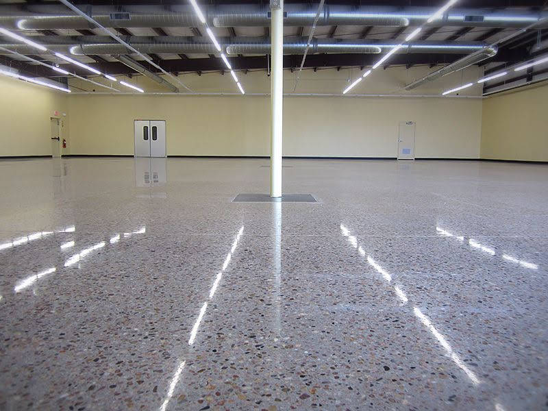 Empty indoor hall with glossy speckled floor, beige walls, white doors, and overhead lights.