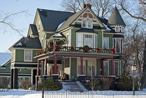A large green house with christmas decorations on the porch