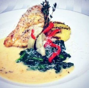 Chicken breast with spinach, peppers, artichoke, and polenta, on a white plate.