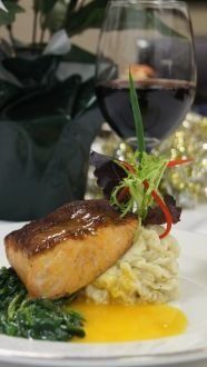 Pan-seared salmon on mashed potatoes, spinach, and sauce, with wine glass in background.