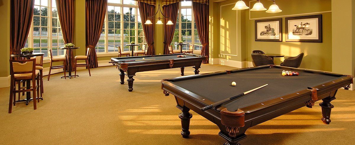 A pool room with two billiard tables, windowed walls, and bar stools.