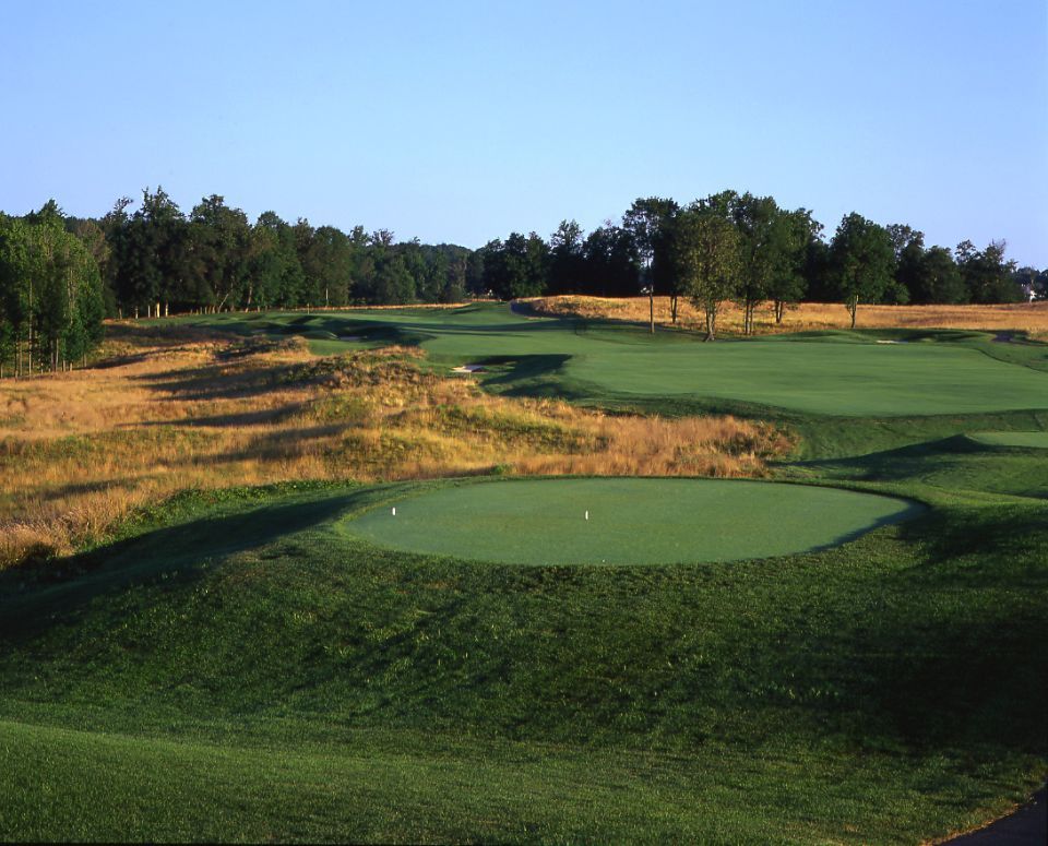 Green golf course with putting green, fairways, and surrounding grassy rough.