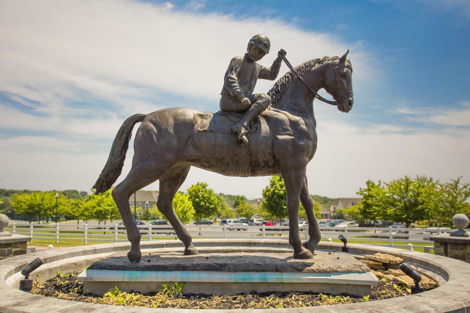 Bronze statue of a jockey on a horse in a round fountain, set in a sunny park.