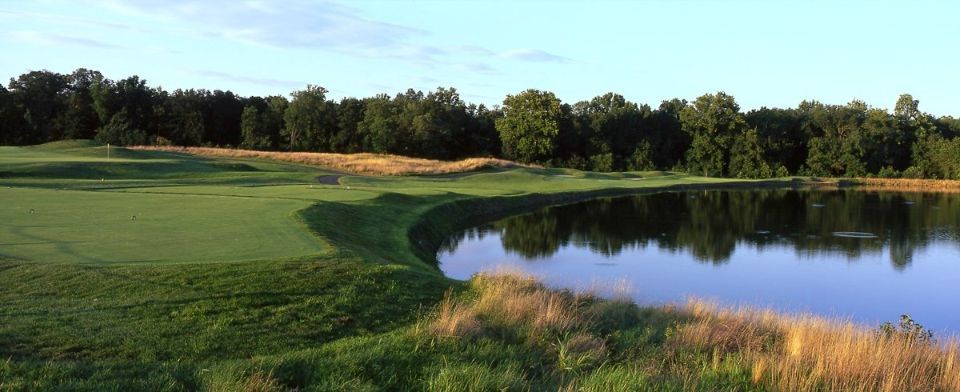 Golf course green with lake in the foreground and trees in the background.