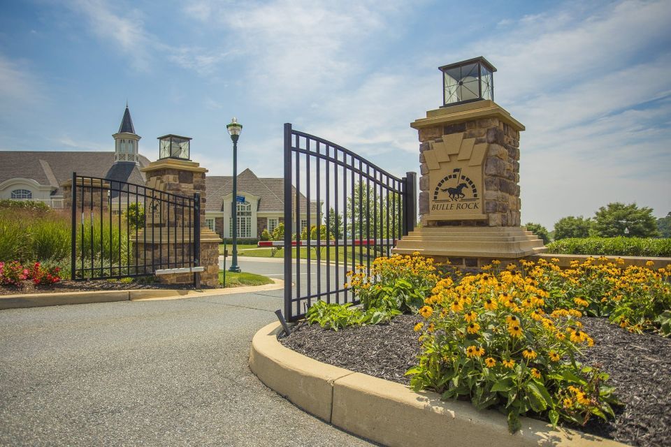 Entrance gate to a community with stone pillars, black iron gates, and yellow flowers.