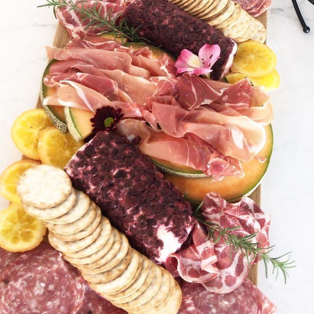 A variety of meats and crackers on a wooden cutting board