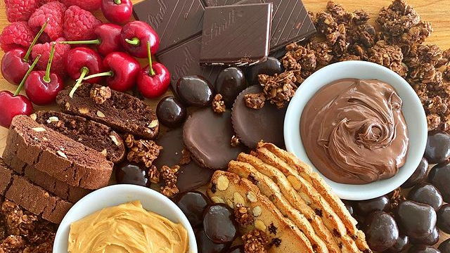 A wooden table topped with a variety of chocolates , cookies , and berries.